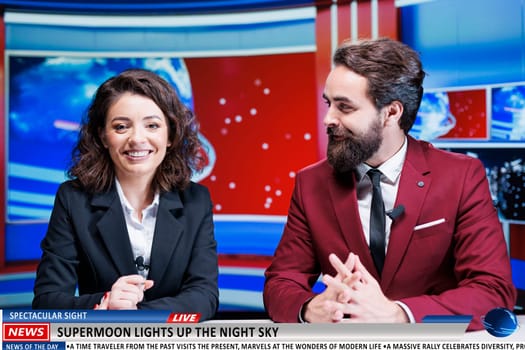 TV reporters talk about supermoon wonder in newsroom, news anchor team on morning show revealing information about magical astronomy sight. Man and woman journalists on live segment.