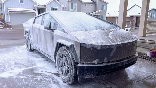 A Tesla Cybertruck undergoes a thorough wash, its unique and angular exterior covered in soap suds, highlighting the vehicle sleek design and durable surfaces.