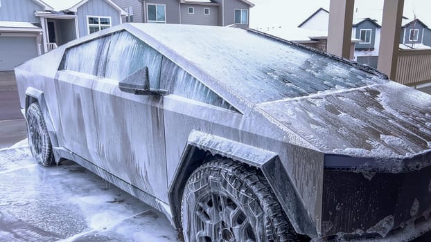 A Tesla Cybertruck undergoes a thorough wash, its unique and angular exterior covered in soap suds, highlighting the vehicle sleek design and durable surfaces.