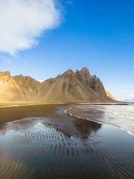 Drone shot of vestrahorn mountains on famous beach with spectacular black sand on stokksnes peninsula. Atlantic ocean coastline beachfront and rocky hills creating majestic surroundings.