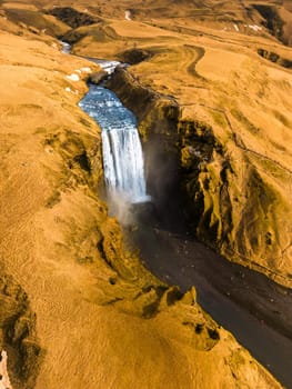 Aerial view of grand glacial skgafoss waterfall gushing down of frigid slopes in Iceland, natural landscape. Major cascade in nordic countries, falling off of brown hillsides.