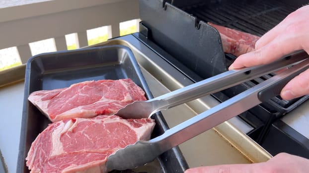 This image showcases the art of grilling, featuring three thick steaks cooking on a barbecue grill, with a row of foil-wrapped corn on the cob above, capturing a typical scene of a hearty outdoor meal preparation.