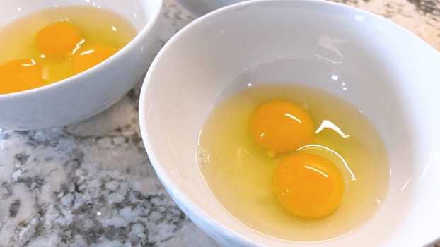 This image showcases three raw eggs cracked into a white bowl, set on a marble countertop, ready for mixing or cooking, highlighting the simplicity and beauty of basic cooking ingredients.