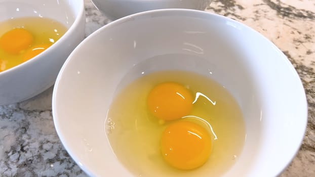 This image showcases three raw eggs cracked into a white bowl, set on a marble countertop, ready for mixing or cooking, highlighting the simplicity and beauty of basic cooking ingredients.