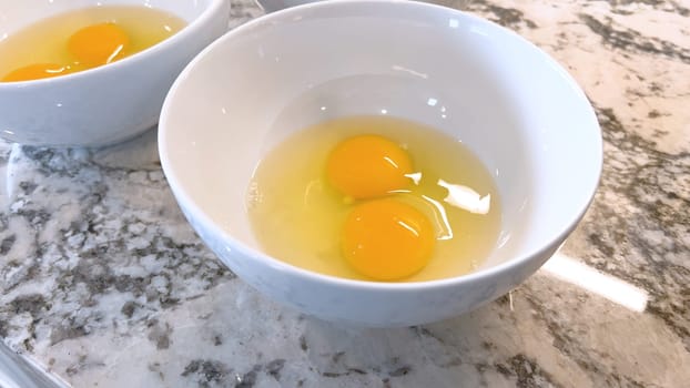 This image showcases three raw eggs cracked into a white bowl, set on a marble countertop, ready for mixing or cooking, highlighting the simplicity and beauty of basic cooking ingredients.