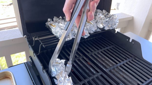 Several ears of corn wrapped in aluminum foil are lined up on a barbecue grill, slowly roasting to perfection, showcasing a popular and delicious method of cooking this classic side dish.