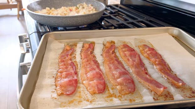 This image features juicy strips of bacon cooking in the oven on a parchment-lined baking tray, capturing the appealing golden-brown color and the enticing aroma as it crisps up.