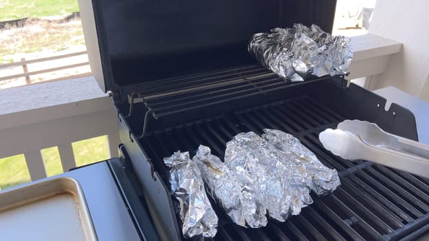 Several ears of corn wrapped in aluminum foil are lined up on a barbecue grill, slowly roasting to perfection, showcasing a popular and delicious method of cooking this classic side dish.