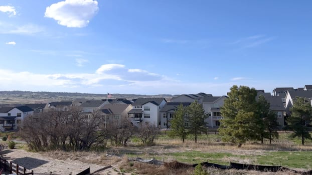 This image captures a serene suburban setting, showcasing a row of modern homes with distinct architectural styles, set against a backdrop of a clear blue sky and surrounded by natural greenery.