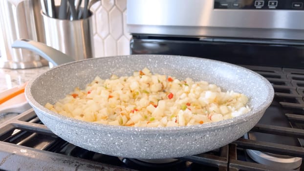 A frying pan on a gas stove sizzles with diced potatoes and colorful bits of red and green peppers, showcasing a delicious and simple home-cooked side dish in the making.