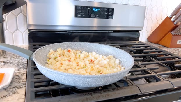 A frying pan on a gas stove sizzles with diced potatoes and colorful bits of red and green peppers, showcasing a delicious and simple home-cooked side dish in the making.