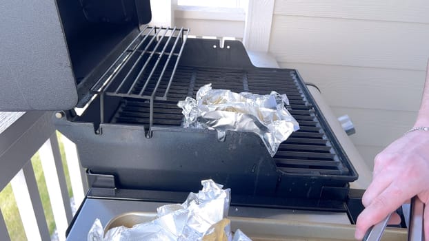 Several ears of corn wrapped in aluminum foil are lined up on a barbecue grill, slowly roasting to perfection, showcasing a popular and delicious method of cooking this classic side dish.