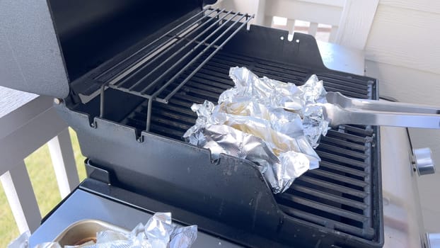 Several ears of corn wrapped in aluminum foil are lined up on a barbecue grill, slowly roasting to perfection, showcasing a popular and delicious method of cooking this classic side dish.