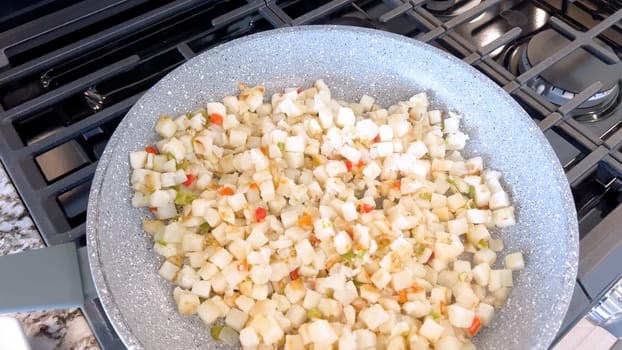 A frying pan on a gas stove sizzles with diced potatoes and colorful bits of red and green peppers, showcasing a delicious and simple home-cooked side dish in the making.