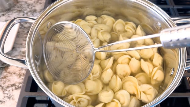 A large pot filled with boiling tortellini pasta showcases the preparation of this traditional Italian dish, with the pasta floating in water ready to be served, set on a modern gas stove.