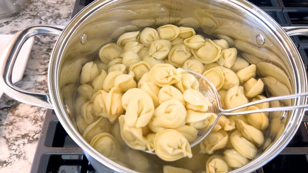 A large pot filled with boiling tortellini pasta showcases the preparation of this traditional Italian dish, with the pasta floating in water ready to be served, set on a modern gas stove.