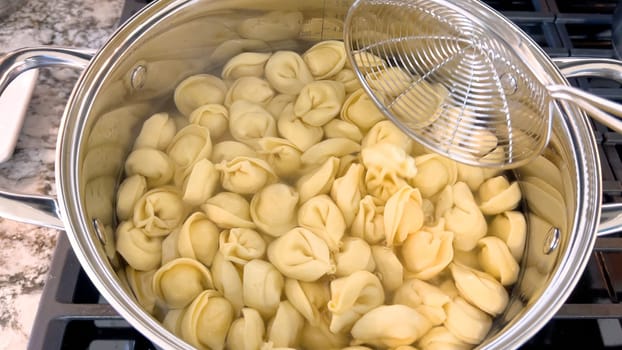 A large pot filled with boiling tortellini pasta showcases the preparation of this traditional Italian dish, with the pasta floating in water ready to be served, set on a modern gas stove.