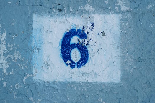 Number six painted on a blue scratched wall in a rectangle with peeling paint. High quality photo