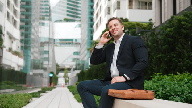 Caucasian businessman sitting at bench while talking to manager by using phone about planning strategy. Professional executive manager calling marketing team and sharing creative idea at city.Urbane.