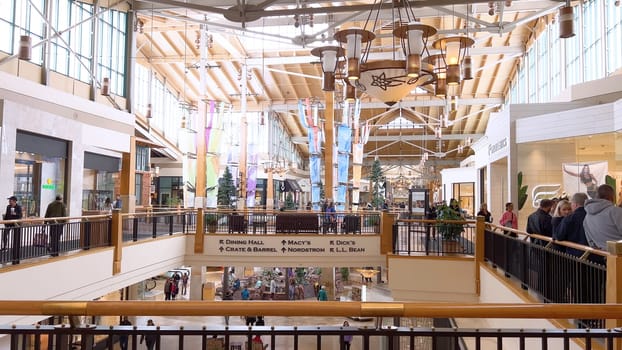 Denver, Colorado, USA-April 28, 2024- Capturing the expansive and airy interior of Park Meadows Mall, this image highlights the modern architectural style with wooden beams, large hanging lights, and a series of vibrant hanging ribbons, creating a lively shopping atmosphere.