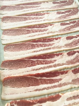 Neatly arranged raw bacon strips on a baking tray, prepared for cooking, capturing the fresh, uncooked look of this popular breakfast ingredient before it turns crispy and golden.