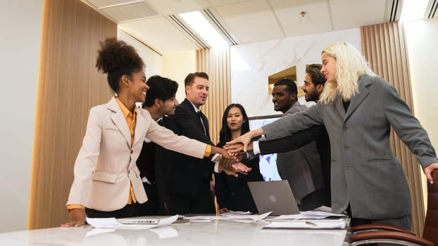 Group of diverse office worker join hand together in ornamented office room symbolize business synergy and strong productive teamwork in workplace. Cooperation and unity between business employee.