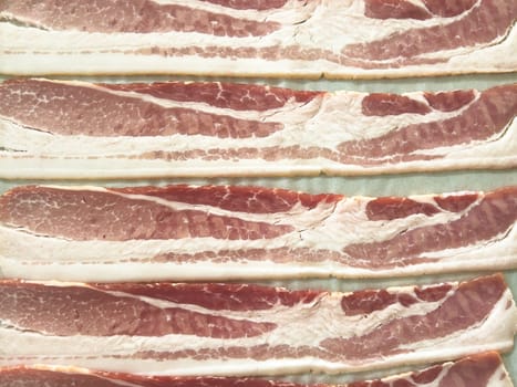 Neatly arranged raw bacon strips on a baking tray, prepared for cooking, capturing the fresh, uncooked look of this popular breakfast ingredient before it turns crispy and golden.