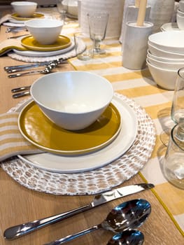 A beautifully arranged dining table featuring modern tableware with a striking color palette of white and gold plates, complemented by striped napkins and clear glassware, set on a wooden table for a stylish meal experience.