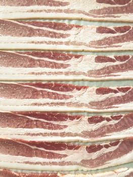 Neatly arranged raw bacon strips on a baking tray, prepared for cooking, capturing the fresh, uncooked look of this popular breakfast ingredient before it turns crispy and golden.
