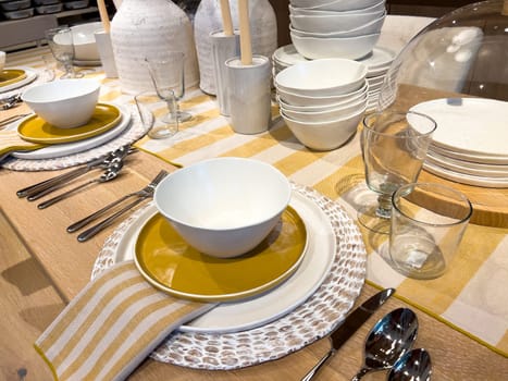 A beautifully arranged dining table featuring modern tableware with a striking color palette of white and gold plates, complemented by striped napkins and clear glassware, set on a wooden table for a stylish meal experience.