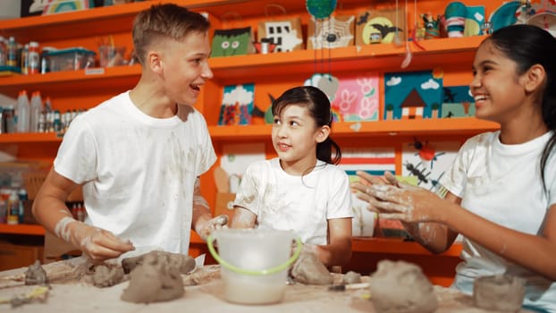 Happy diverse student laughing while caucasian girl modeling cup in pottery class or workshop. Caucasian highschool girl looking at boy while smiling boy attend in art lesson. Education. Edification.