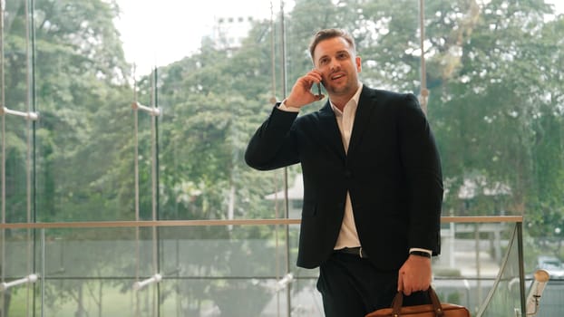 Caucasian businessman calling manager by using smart phone and discuss about financial report. Male leader talking marketing team by using telephone while standing at stair in modern building. Urbane.