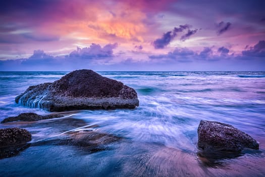 Tropical beach vacation background - waves and rocks on beach on sunset with beautiful cloudscape. Varkala, India