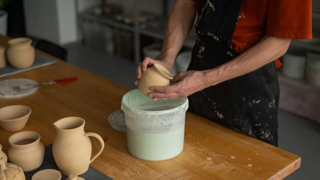 Close-up of a potter's hands glazing a pottery piece