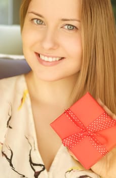 Happy smiling woman holding a red gift box, face portrait with natural make-up and holiday lifestyle at home concept