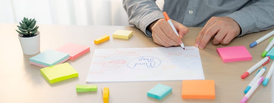 Skilled businessman brainstorms marketing ideas using mind maps. Successful male startup leader drafts financial plan on table with sticky notes scatter around. Closeup. Focus on hand.Variegated.