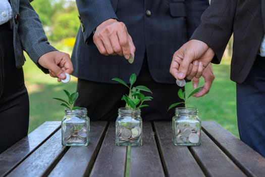 Business people put coin to money saving glass jar on outdoor table as sustainable money growth investment or eco-subsidize. Green corporate promot and invest in environmental awareness. Gyre