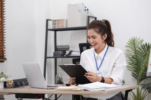 Young business woman meeting on laptop, doing paperwork in white office room.