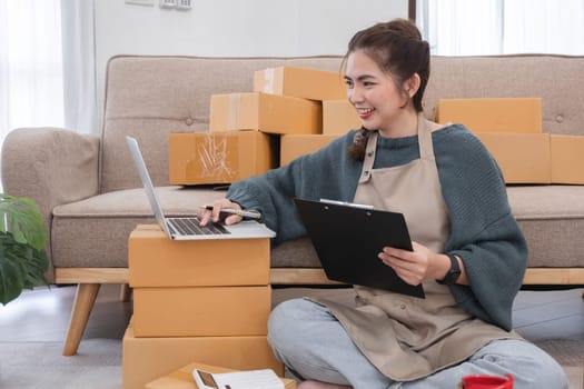 Young woman, small business owner selling products online, accepting online product orders via laptop, sits in a room with boxes of products..