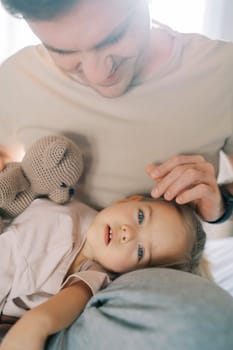 Dad stroking the head of a little girl with a teddy bear lying on his lap. High quality photo