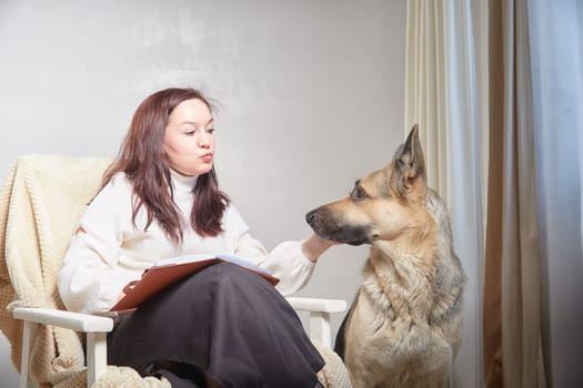 Middle aged Woman Relaxing in Chair With German Shepherd Indoors. Smiling mature woman in armchair with her attentive pet dog in a cozy room