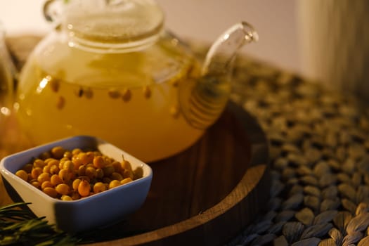 A teapot with sea buckthorn tea, honey and a plate with sea buckthorn on a tray.