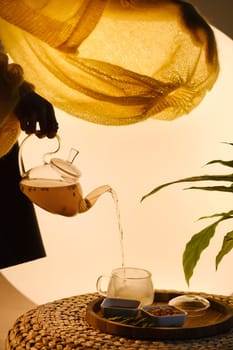 Close-up of a hand with a kettle. A teapot with sea buckthorn tea, honey and a plate with sea buckthorn on a tray.