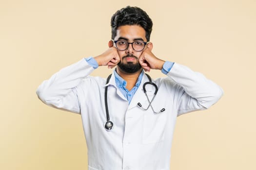 Indian young doctor cardiologist man feeling hopelessness and loneliness, nervous breakdown, loses, bad fortune, loss, unlucky news, fail. Arabian apothecary pharmacy guy isolated on beige background