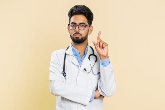 Displeased upset Indian young doctor cardiologist man reacting to unpleasant awful idea, dissatisfied with bad work, wave hand, shake head No dismiss bad idea proposal. Arabian guy on beige background