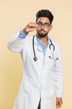 Knock-knock who is there. Excited Indian doctor cardiologist man knocking door gesture asking who is at home, being clueless uncertain. Hello, welcome. Arabian apothecary on beige background. Vertical