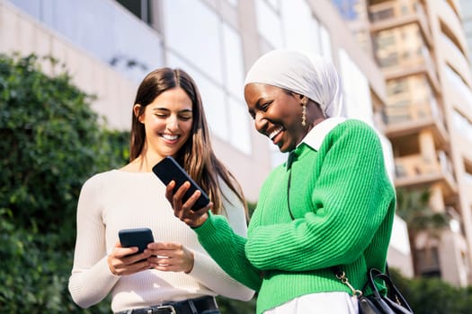 two young female friends smiling happy looking their mobile phones, concept of friendship and technology