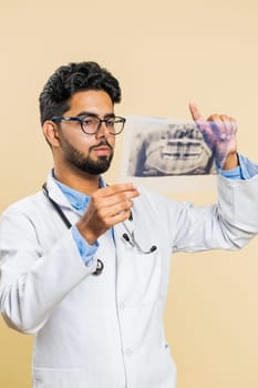 Indian young doctor orthodontist man examines a panoramic x-ray picture of the jaw teeth. 3D model of the patient's mouth, MRI scan. Dentistry, oral care. Arabian stomatology guy on beige background