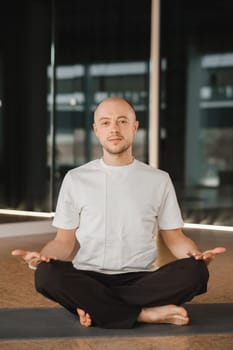 An athletic young man does exercises in the fitness room. A professional guy does yoga in the gym.