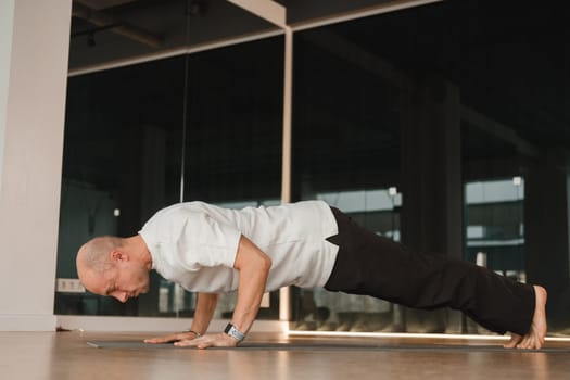 An athletic young man does exercises in the fitness room. A professional guy does yoga in the gym.